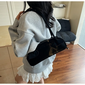 Close-up of a black glossy leather baguette bag worn over the shoulder by a model