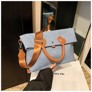 Detail of blue denim tote bag with brown leather handles and adjustable shoulder strap