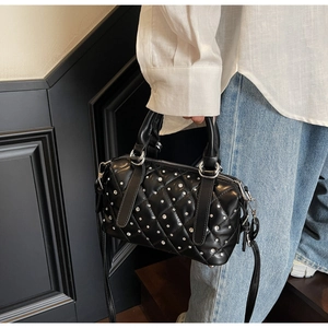Close-up of black quilted Boston bag with silver studs and chain strap on a white shirt
