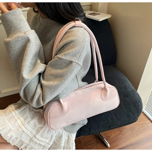 Detail of light pink faux leather shoulder bag worn by model in casual indoor setting