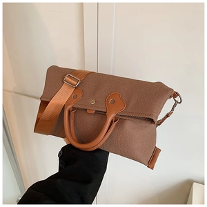 Close-up of brown canvas handbag featuring leather handles and adjustable shoulder strap