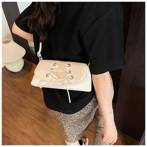 Close-up of cream-colored shoulder bag with lace-up detail worn by model in home setting