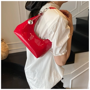 Détail du sac croissant en cuir verni rouge avec chaîne argentée porté à l'épaule