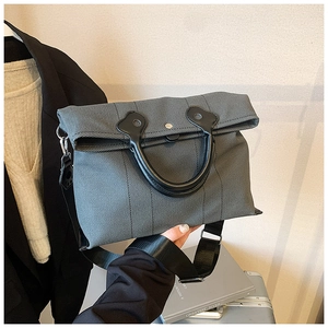 Detail of grey twill canvas bag featuring black leather handles and wide nylon shoulder strap