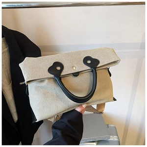 Detail of minimalist beige canvas tote bag featuring black leather handles and metal snap closure