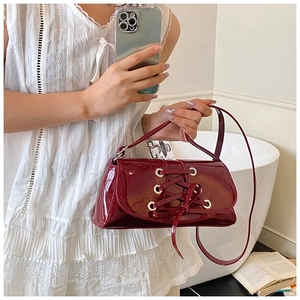 Detail of dark red patent leather shoulder bag with silver eyelets and lace-up straps