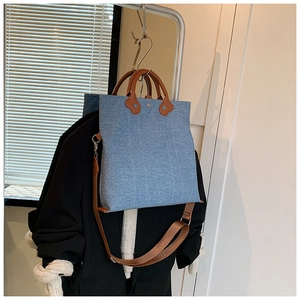 Detail of blue denim canvas tote bag with brown leather handles and vertical stitching