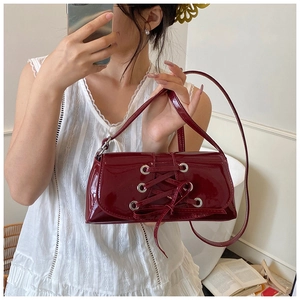 Detail of burgundy patent leather baguette bag with lace-up straps and metal eyelets