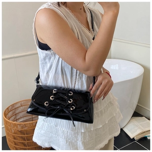 Close-up of black patent leather underarm bag with stylish strap details and silver eyelets