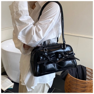 Detail of glossy black patent shoulder bag featuring decorative bow pockets and silver buckles