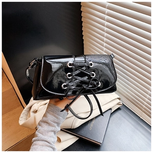 Close-up of black patent leather bag featuring silver eyelets and lace-up bow detail