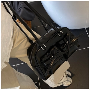 Close-up of black glossy shoulder bag with front bow pockets and mirror-like finish