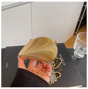 Nahaufnahme der goldfarbenen Muschel-Abendtasche mit Wellenstruktur und Perlenkette