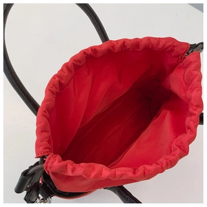 Detail of red fabric lining and drawstring closure on a black minimalist straw tote bag