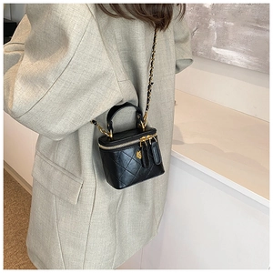 Detail of black quilted mini crossbody bag with gold chain strap on grey blazer
