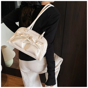 Detail of white glossy leather shoulder bag with decorative bows and twin handles