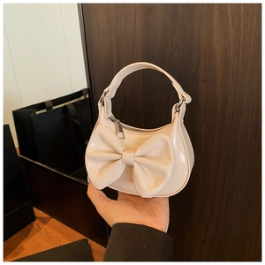 Detail einer cremeweißen Mini-Handtasche mit großer Schleife und glänzendem Lackleder