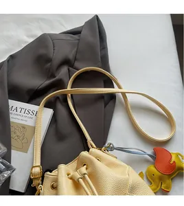 Detail of beige litchi grain leather bucket bag with drawstring and elephant charm