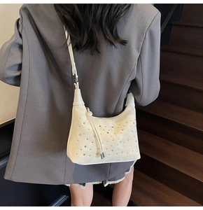 Detail of creamy white ruched shoulder bag featuring sparkling rhinestone studs and leather strap