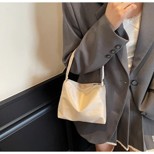 Close-up of cream-colored fabric shoulder bag with metal zipper worn with grey blazer