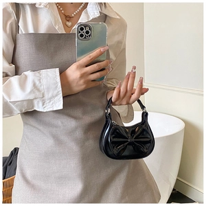 Detail einer Mini-Handtasche in Schwarz mit Schleife und Glanz-Optik, präsentiert am Modell