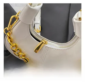 Close-up of shiny white crescent bag featuring thick gold chain strap and polished zipper