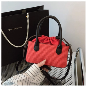 Detail of red straw woven handbag with black leather handles and drawstring closure