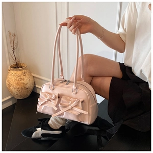 Close-up of pink glossy shoulder bag featuring delicate bow knots and dual front pockets