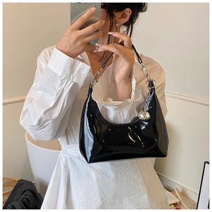 Sac hobo chic en cuir verni noir avec breloque argentée porté par un mannequin en blanc