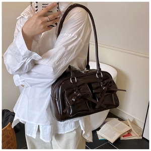 Detail of dark brown patent leather shoulder bag with decorative bows and twin front pockets