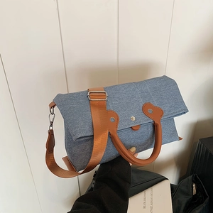 Blue denim tote bag with brown leather handles and wide shoulder strap on wooden background