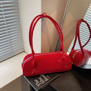 Glossy red cylindrical baguette bag with silver zipper on a minimalist book set