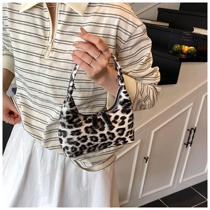 Close-up of leopard print patent leather dumpling bag held by a model in casual attire