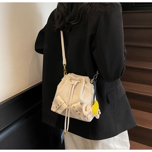 White bucket bag with elephant charm and studs worn by a model in minimalist setting