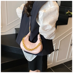 Detail shot of a pink patent leather hobo bag with a gold chain strap on a model