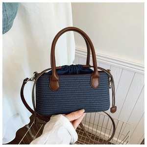 Close-up of navy blue woven tote bag with brown leather handles and drawstring closure