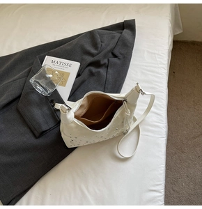 Top view of white ruched hobo bag with silver studs on a stylish bed setting
