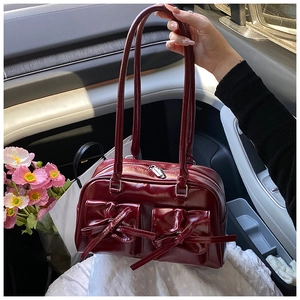 Close-up of deep red patent leather shoulder bag with decorative bow flap pockets