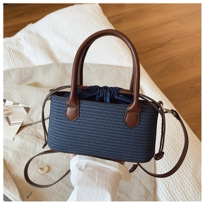 Detailed view of the dark blue woven handbag with brown leather handles and drawstring closure