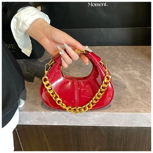 Detail of red glossy patent leather dumpling bag with chunky gold chain strap