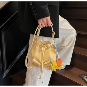 Detail of beige drawstring bucket bag with yellow elephant charm and gold hardware