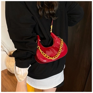 Detail of red patent leather dumpling bag with chunky gold chain strap on black outfit