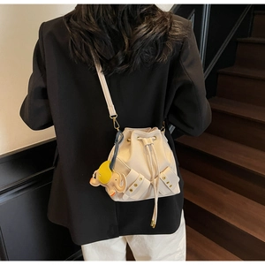 Detail of cream bucket bag with drawstring and elephant charm on model back view