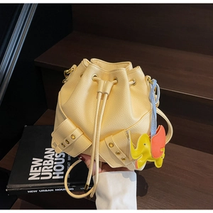 Macro view of yellow litchi leather bucket bag with gold rivets and elephant charm