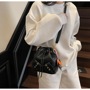 Detail of black drawstring bucket bag with gold eyelet pockets and leaf charm