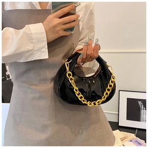 Detail of glossy black patent leather dumpling bag with chunky gold chain handle