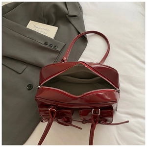 Detail view of burgundy patent leather bag showing zipper opening and interior storage