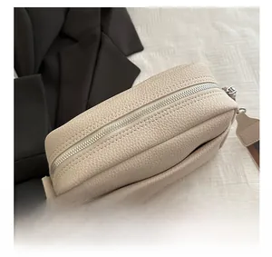 Detail of silver smooth zipper and striped fabric strap on beige lychee leather bag