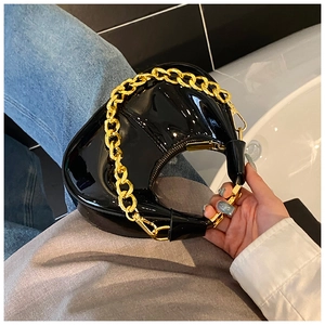 Close-up of black patent leather dumpling bag with chunky gold chain handle detail
