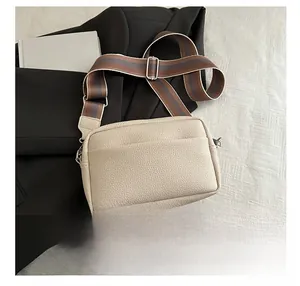 Detail showing beige litchi grain texture and wide striped strap of this square crossbody bag